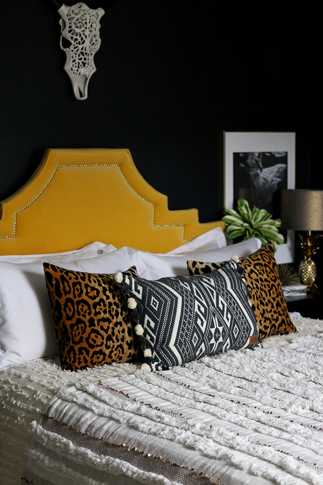 black bedroom with yellow velvet headboard and leopard print cushions