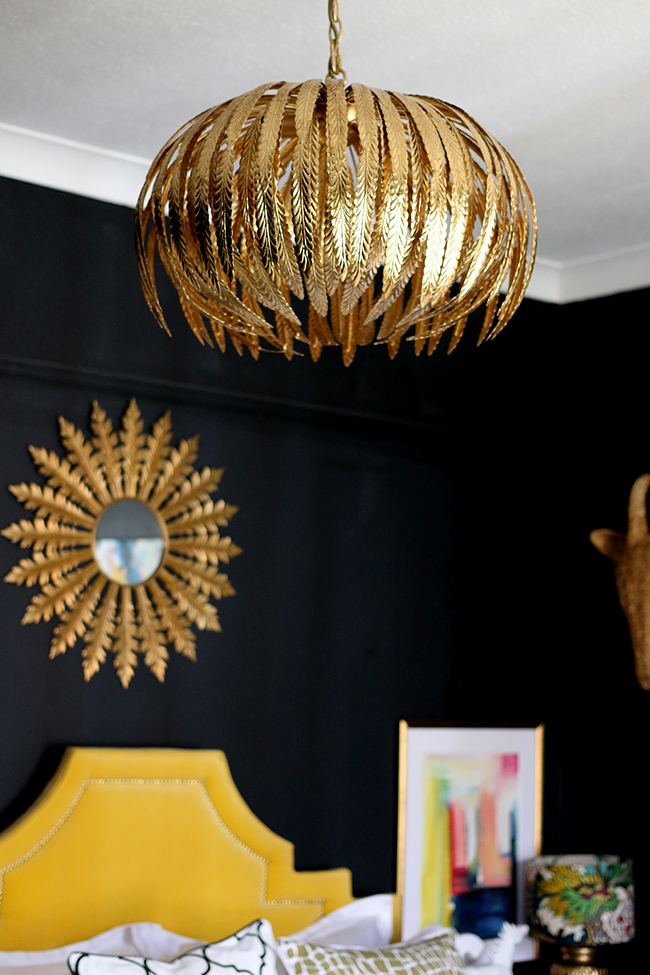 black bedroom with gold light fixture, yellow headboard and colourful artwork - see more on www.swoonworthy.co.uk