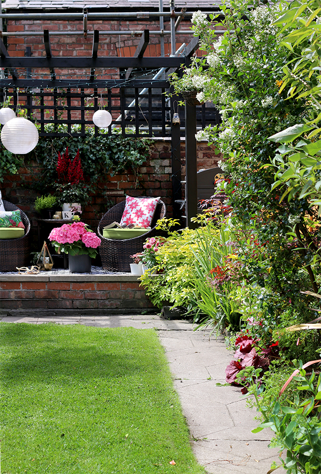 English garden with black pergola and decking area in pink and green