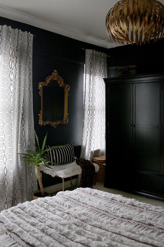 black walls with ornate mirror and brass bench with patterned curtains
