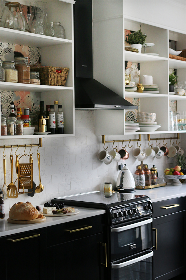 kitchen with black cupboards with white open shelving, marble tiles and brass accents