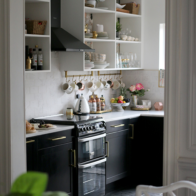 kitchen with black cupboards with white open shelving, marble tiles and brass accents
