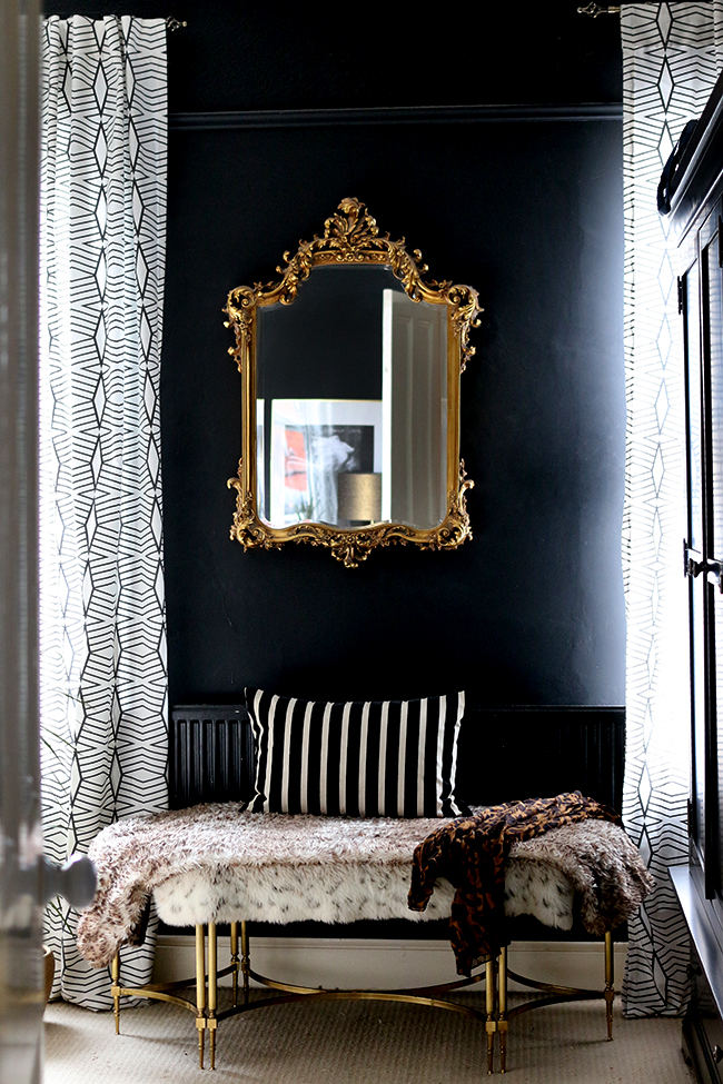black bedroom with ornate gold mirror and gold bench