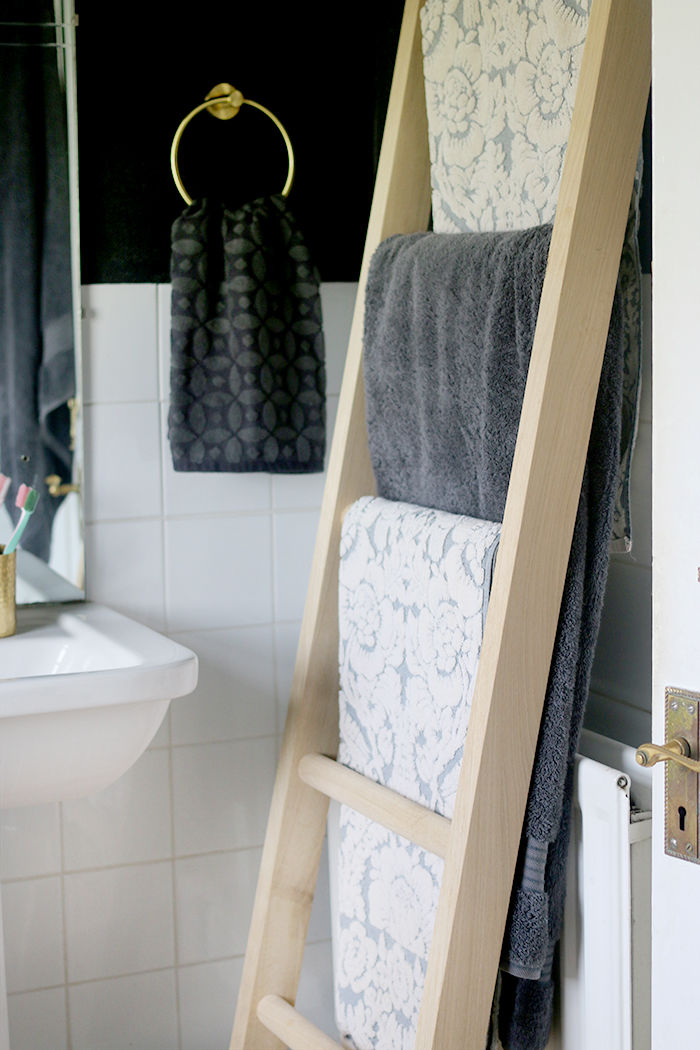 Wooden towel ladder rail in a black bathroom with brass accents