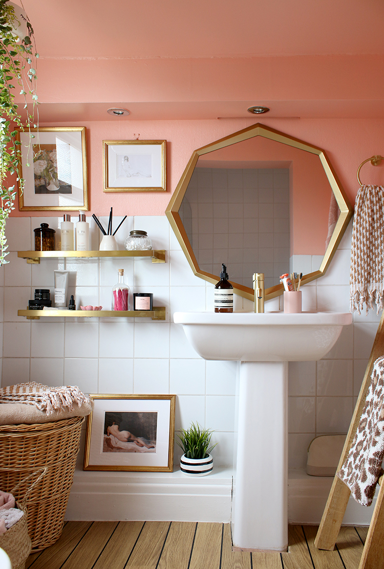 peach bathroom in Victorian home with gold octagon mirror and brass shelving