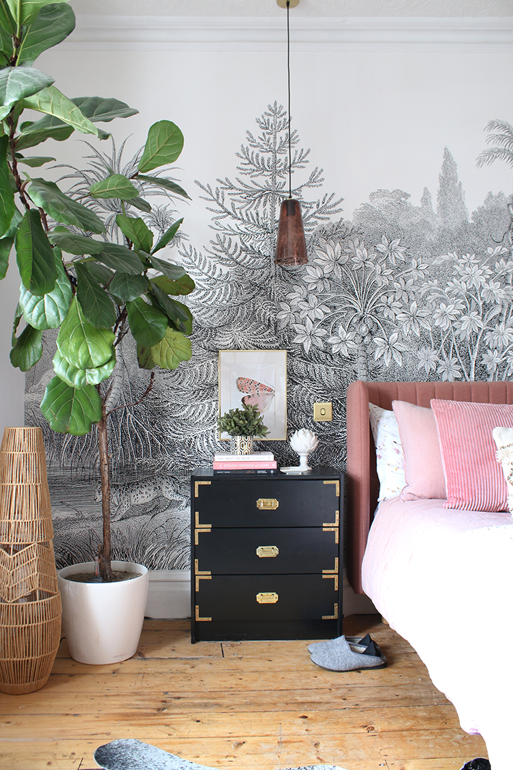 bedroom with black bedside table and fiddle leaf fig with pink bed and wall mural