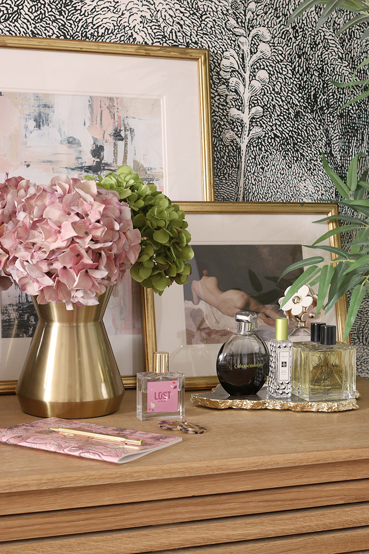 wood bedside table styled with pink flowers small artwork and perfumes